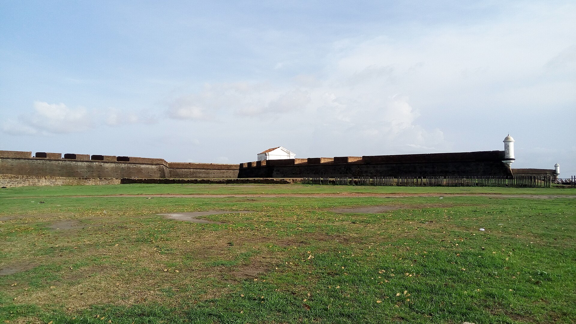 Muralhas de pedra e guarita branca da Fortaleza de São José de Macapá, com gramado à frente.