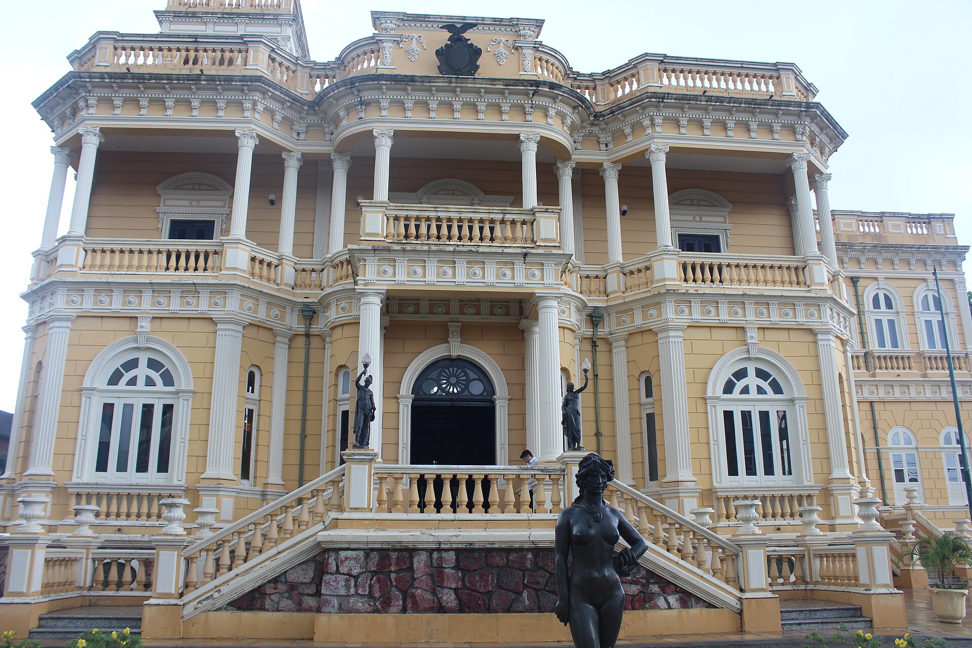 Fachada ocre do Palácio Rio Negro em Manaus, escadaria e estátuas à frente.